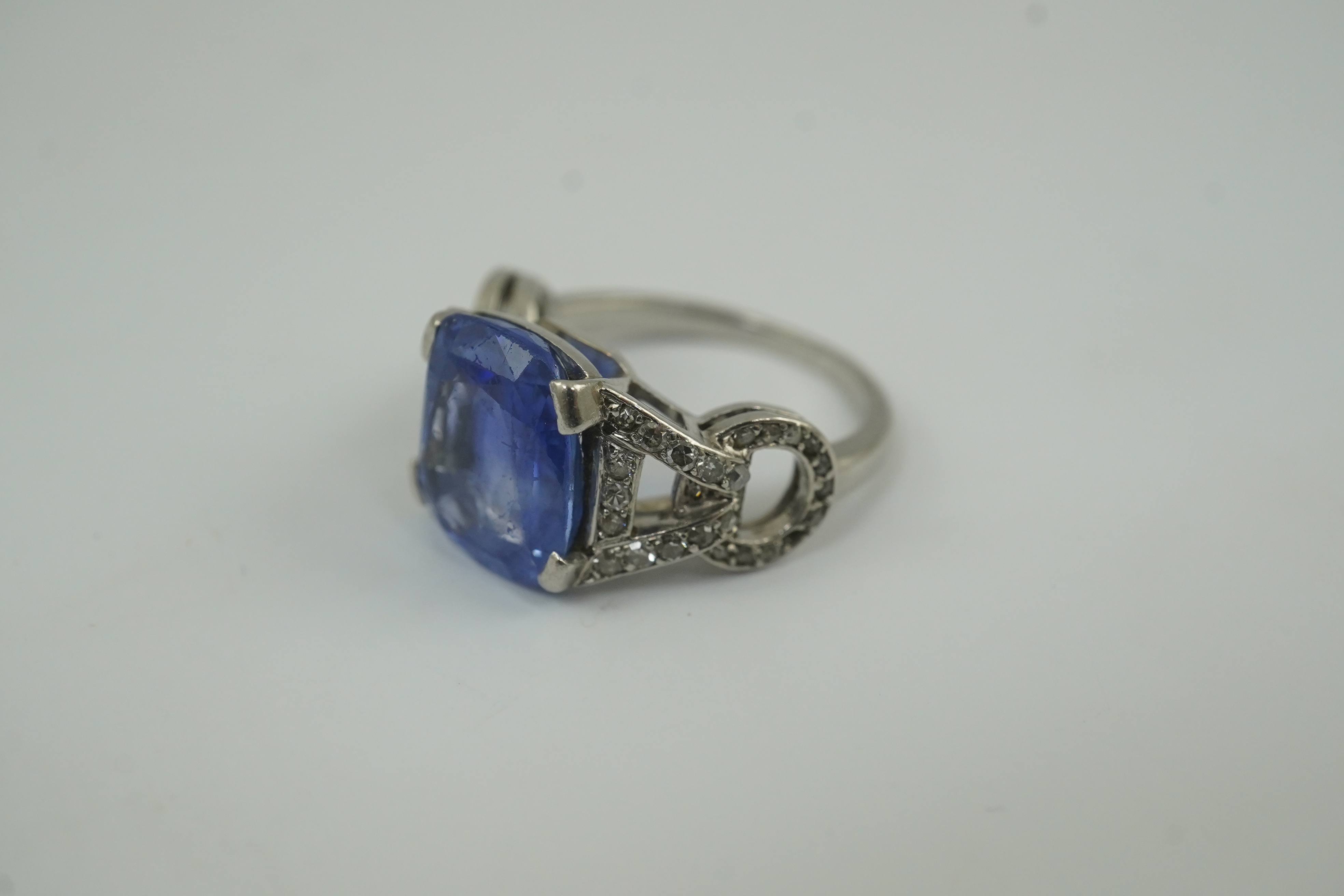 A mid to late 20th century platinum and single stone tapered cushion cut sapphire set dress ring, with diamond chip set pierced shoulders